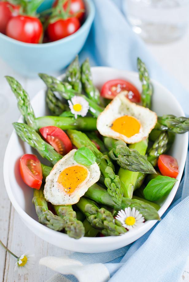 Ein Teller mit Spargel, halbierten Tomaten und Spiegeleiern, garniert mit Basilikum und Gänseblümchen.