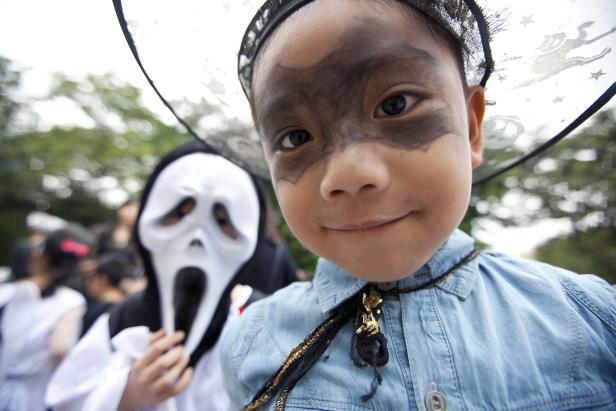 Ein Kind mit Schminke und Hexenhut, im Hintergrund eine Person mit Scream-Maske.