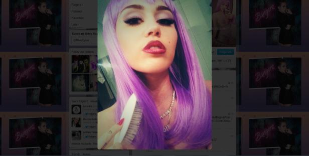 Eine Frau mit lila Perücke bürstet ihre Haare vor einem Bildschirm mit Miley Cyrus-Bildern.