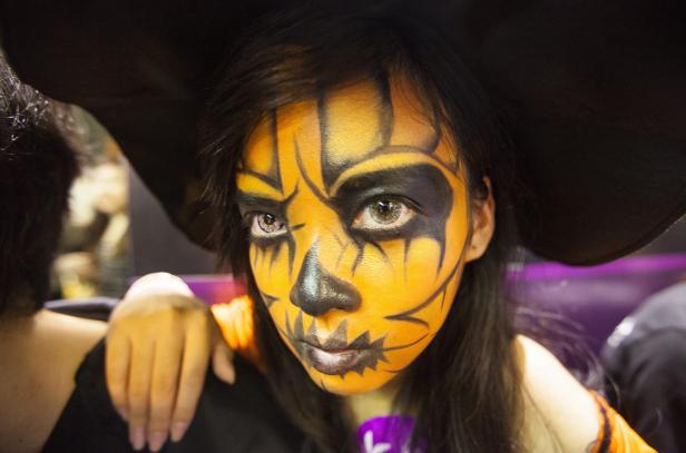 Eine junge Frau mit Kürbis-Gesichtsbemalung und einem schwarzen Hut für Halloween.