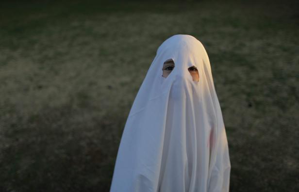 Ein Kind verkleidet als Geist mit einem weißen Laken vor einem Rasen.
