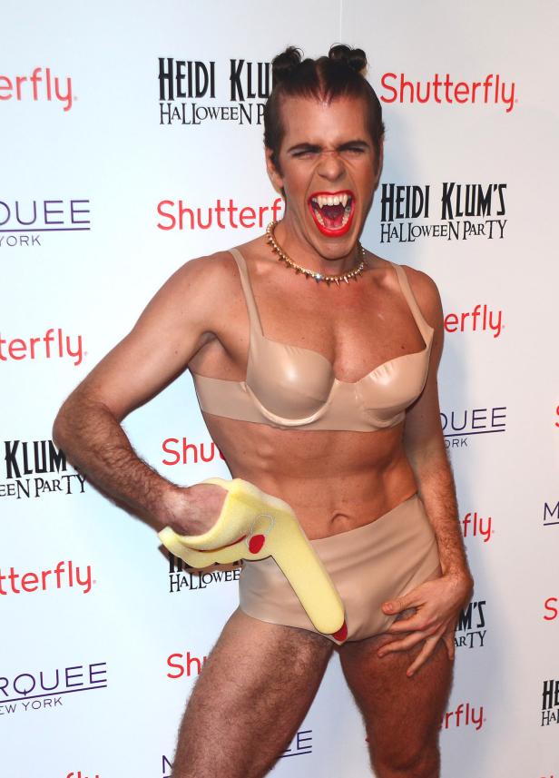 Ein Mann im Halloween-Kostüm mit Vampirzähnen und einer gelben Requisite posiert.