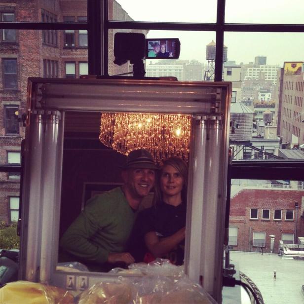 Ein Mann mit Hut und eine Frau posieren vor einem Spiegel mit einem Kronleuchter im Hintergrund.