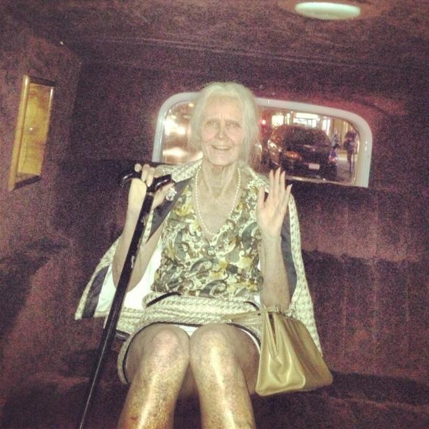 Eine ältere Dame sitzt in einem Auto, lächelt und winkt.