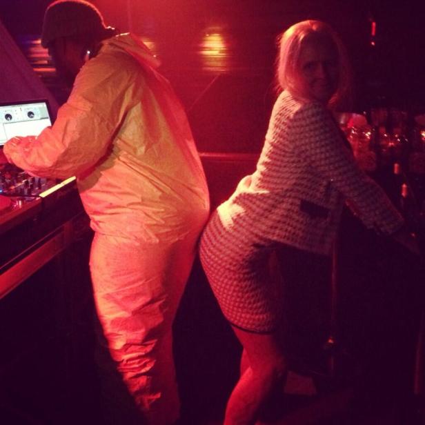 Ein DJ im gelben Schutzanzug legt Musik auf, während eine Frau an seinem Rücken tanzt.