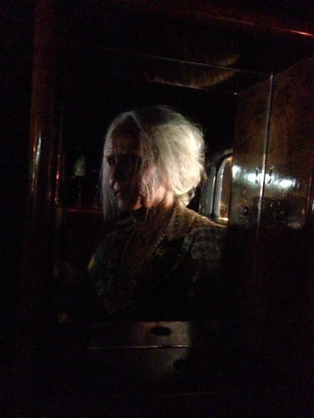 Eine ältere Frau mit weißen Haaren sitzt im Dunkeln in einem Auto.