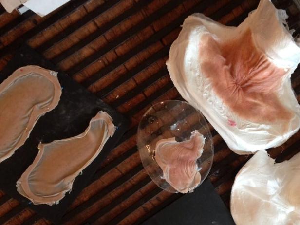 Mehrere Silikonmasken und Gesichtsteile liegen auf einer dunklen Oberfläche.