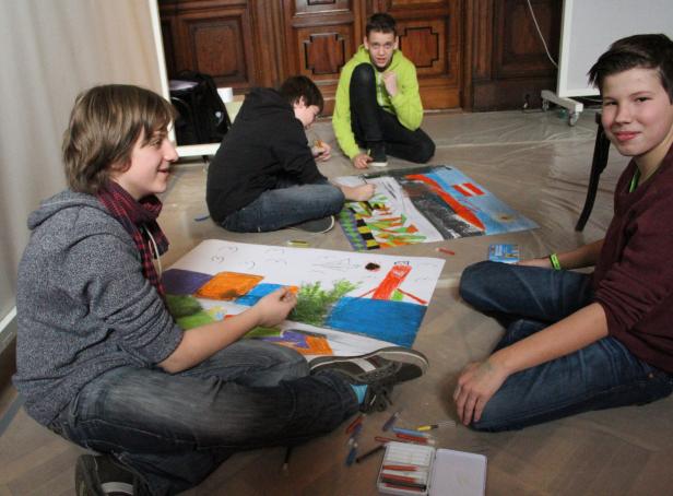Vier Jugendliche sitzen auf dem Boden und malen mit Wachsmalstiften auf Papier.