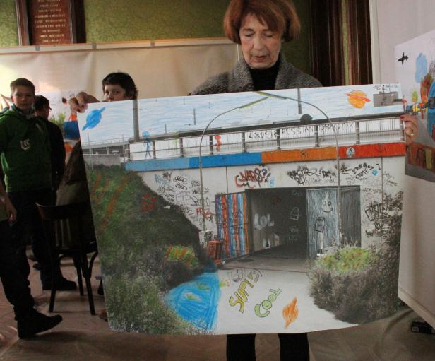 Eine Frau hält eine Zeichnung von einer Unterführung mit Graffiti und dem Schriftzug „Supi Cool“.