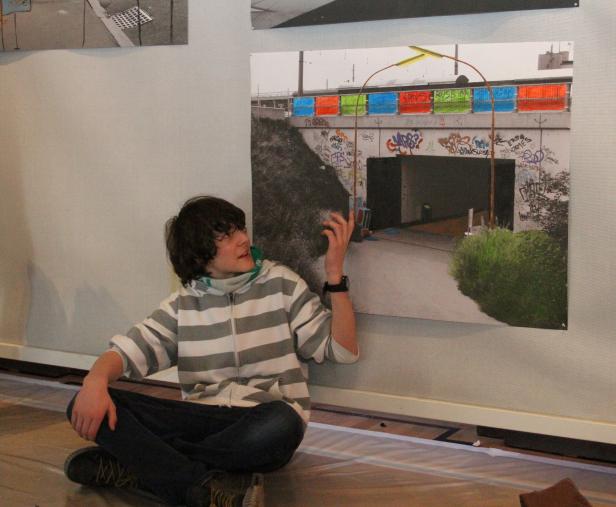 Ein junger Mann sitzt vor einem Foto einer mit Graffiti bemalten Brücke.