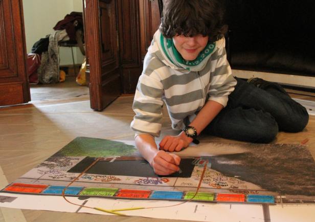 Ein Jugendlicher sitzt auf dem Boden und malt ein farbenfrohes Bild.