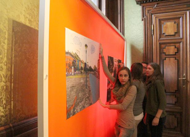 Eine Gruppe von Menschen betrachtet ein farbenfrohes Stadtbild auf einem Plakat.