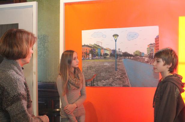 Eine Frau, ein Mädchen und ein Junge betrachten ein Bild mit einer bunten Stadtlandschaft.