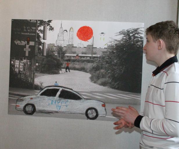 Ein Junge steht vor einem bearbeiteten Schwarzweißfoto mit Zeichnungen, darunter ein Polizeiauto und ein UFO.