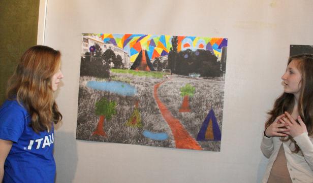 Zwei junge Frauen betrachten ein farbenfrohes Landschaftsbild mit Häusern und Bäumen.