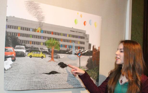 Eine junge Frau zeigt auf ein bearbeitetes Foto eines Gebäudes mit bunten Fenstern und Autos.