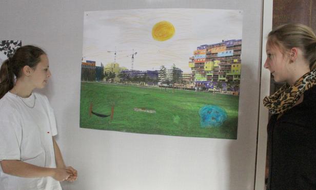 Zwei junge Frauen betrachten ein farbenfrohes Bild von einem Park mit Gebäuden im Hintergrund.