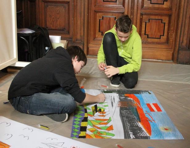 Zwei Jugendliche sitzen auf dem Boden und malen ein großes Bild mit bunten Stiften.