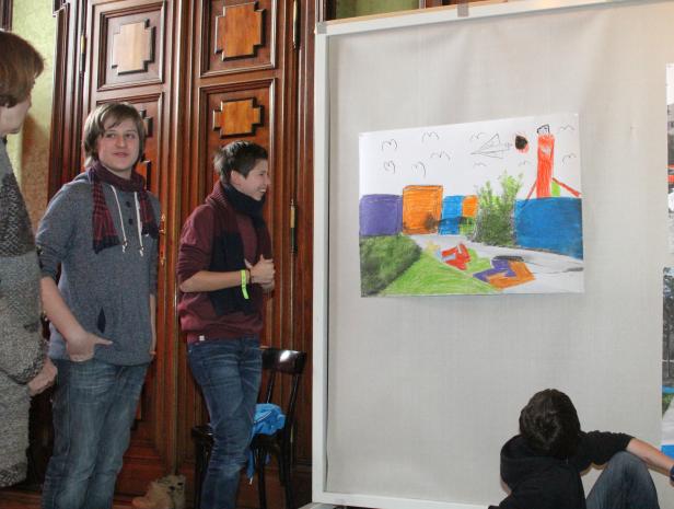 Zwei Jugendliche betrachten ein Kinderbild mit Häusern und einem Flugzeug.