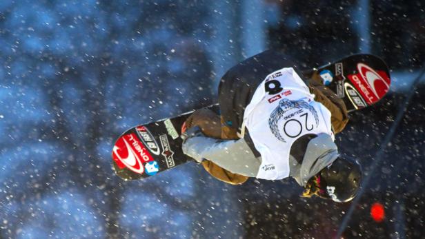 Ein Snowboarder macht bei Schneefall einen Trick in der Luft.
