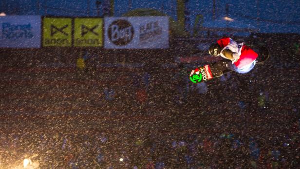 Ein Snowboarder springt vor einer Zuschauermenge in der Nacht.