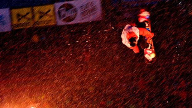 Ein Snowboarder springt in der Luft vor dem Hintergrund von Werbebannern.