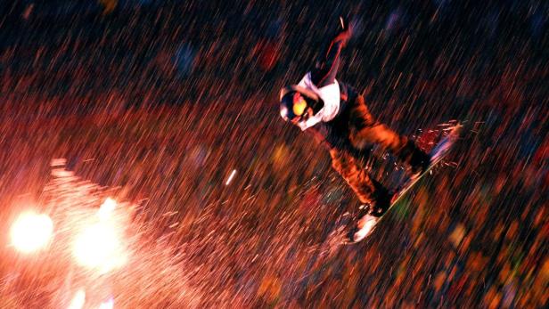 Ein Snowboarder springt im Dunkeln vor einem Publikum, während es regnet.