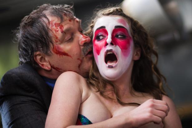 Ein Mann mit Blut im Gesicht umarmt eine Frau mit weiß-roter Gesichtsbemalung, die entsetzt schreit.