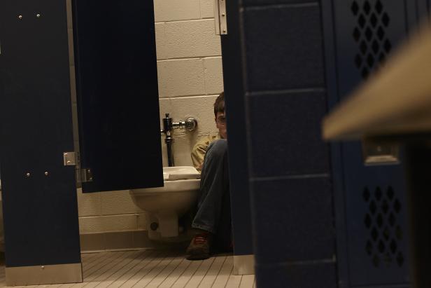 Eine Person sitzt in einer Toilettenkabine in einem öffentlichen Badezimmer.