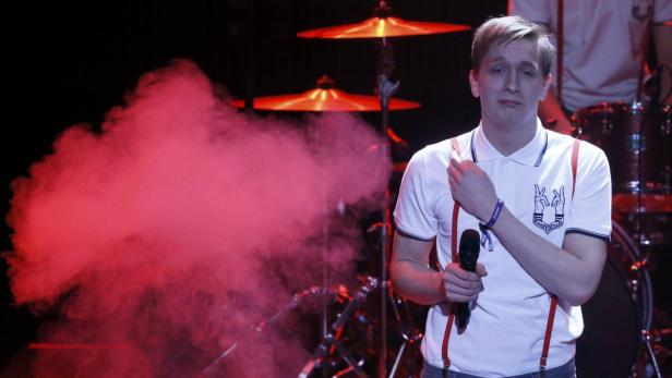 Ein Sänger der Band Kraftklub steht mit Mikrofon vor rotem Rauch auf der Bühne.