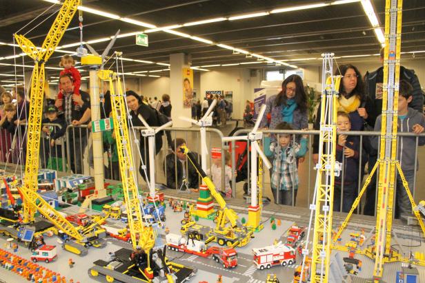 Besucher betrachten eine detailreiche Lego-Landschaft mit Baukränen und Windrädern.