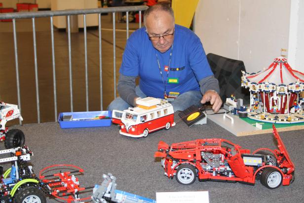 Ein Mann präsentiert detailreiche Modelle aus Legosteinen, darunter ein Karussell und ein roter VW-Bus.