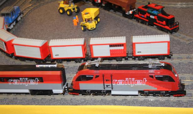 Ein roter Railjet-Zug aus Lego steht auf den Gleisen.