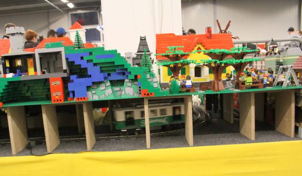 Eine LEGO-Modelllandschaft mit Häusern, Bäumen, Figuren und einer fahrenden Eisenbahn.