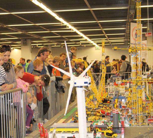 Eine Gruppe von Menschen betrachtet eine detailreiche Lego-Stadt mit Windrad und Kränen.