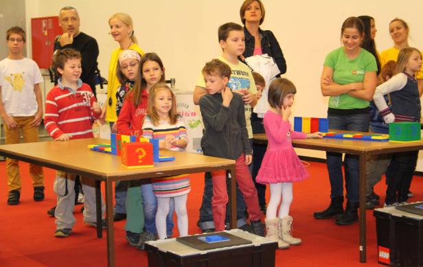 Eine Gruppe Kinder steht an Tischen und spielt mit bunten Bausteinen.