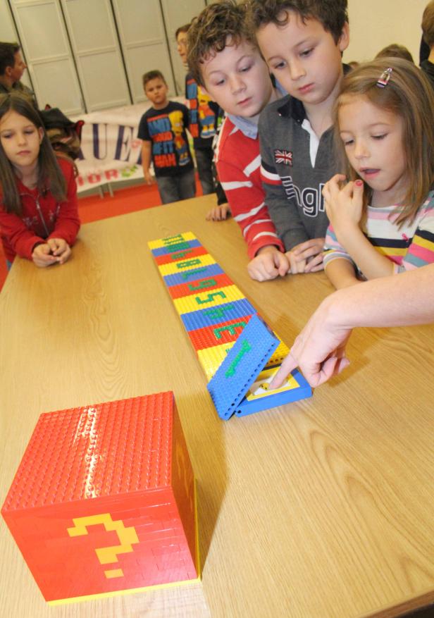 Kinder spielen mit einem Lernspiel aus Legosteinen auf einem Tisch.