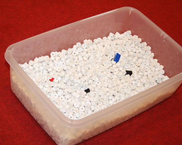 Eine transparente Plastikbox gefüllt mit vielen weißen und einigen farbigen LEGO-Steinen.