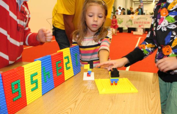 Ein Mädchen spielt mit bunten Legosteinen an einem Tisch.