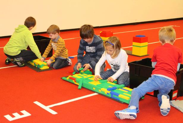 Fünf Kinder spielen mit Legosteinen auf einem roten Teppich.