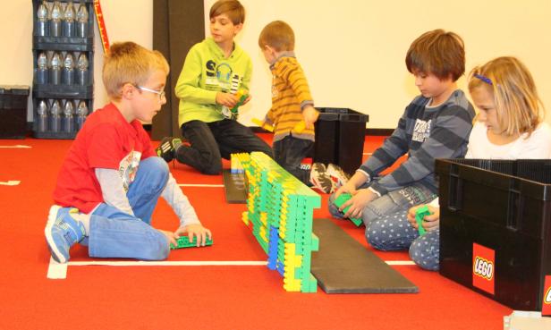Eine Gruppe Kinder spielt mit Legosteinen auf einem roten Teppich.