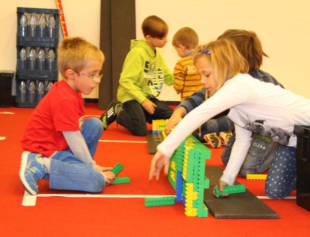 Mehrere Kinder spielen mit bunten Bausteinen auf einem roten Teppich.