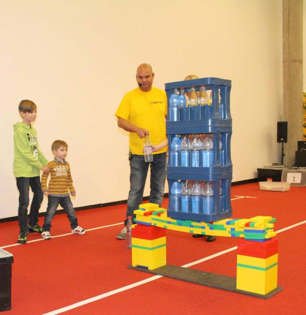 Kinder und ein Mann beim Experimentieren mit einer Brücke aus Legosteinen und Wasserflaschen.