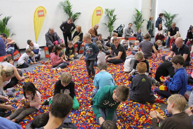 Eine Gruppe von Kindern und Erwachsenen spielt mit Legosteinen.