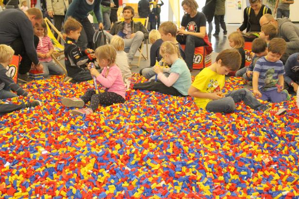 Kinder sitzen in einem Becken voller bunter Legosteine und spielen.
