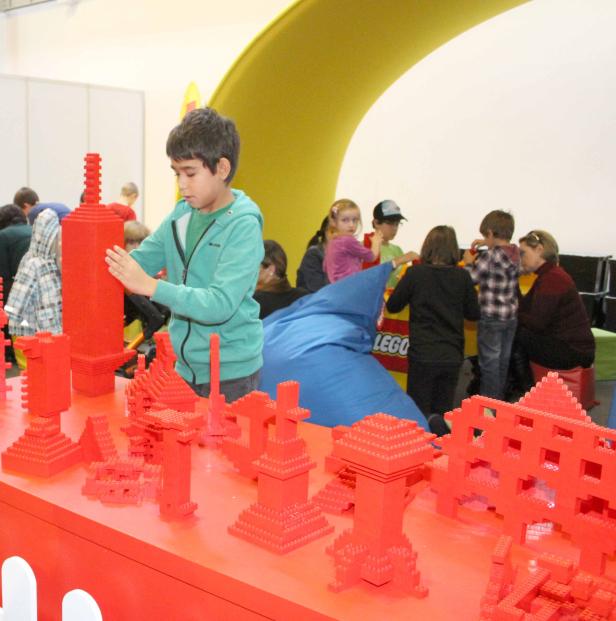 Ein Junge baut mit roten Legosteinen an einem Tisch.