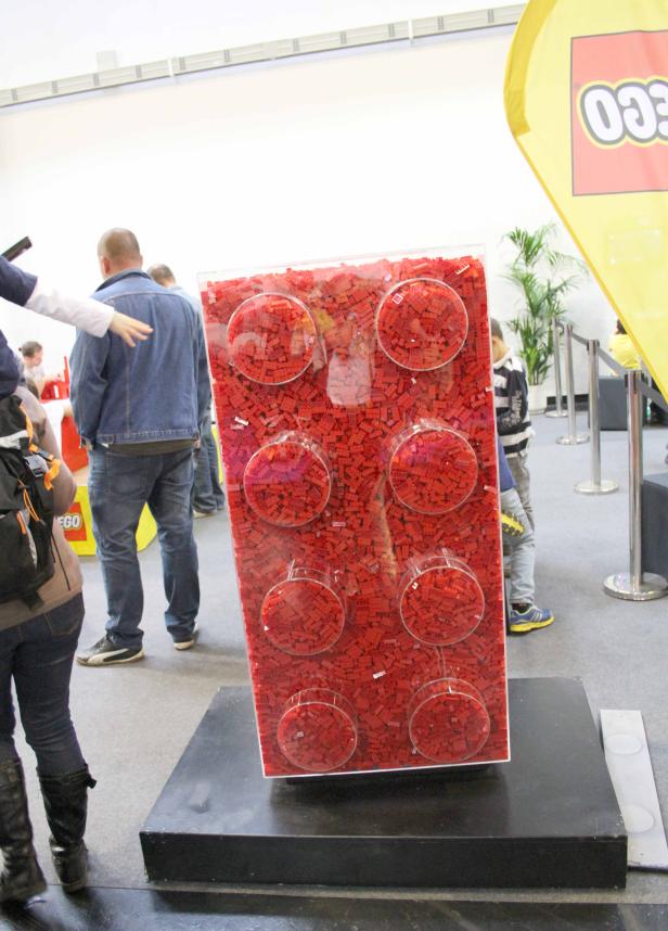 Ein großer, roter Legostein aus vielen kleinen Legosteinen steht auf einem Sockel.