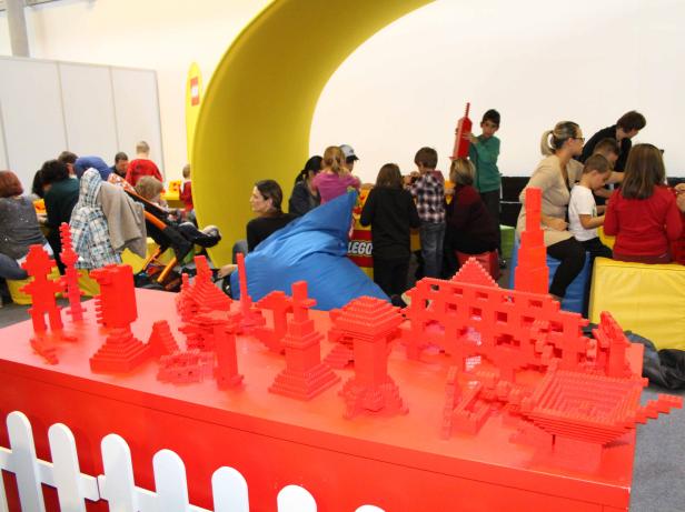 Kinder spielen mit roten Lego-Steinen auf einem Spieletisch.