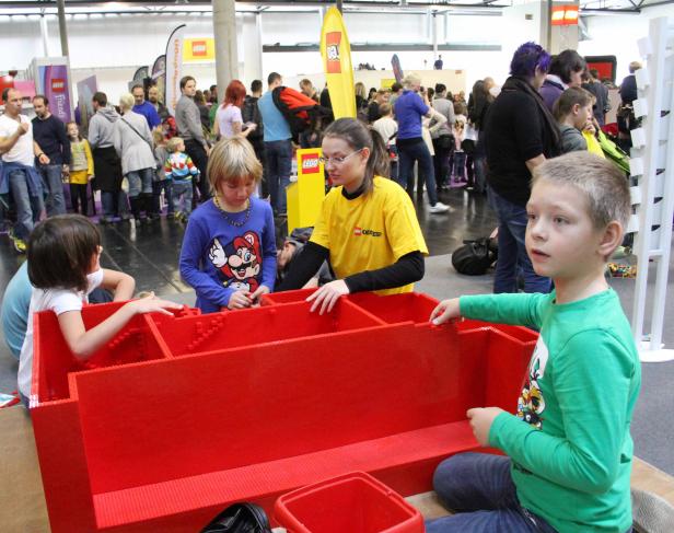 Kinder spielen mit übergroßen roten Legosteinen auf einer Veranstaltung.
