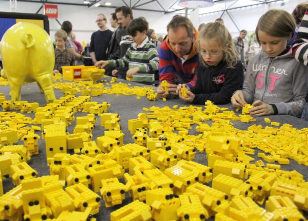 Kinder und Erwachsene bauen gelbe Schweine aus Legosteinen.